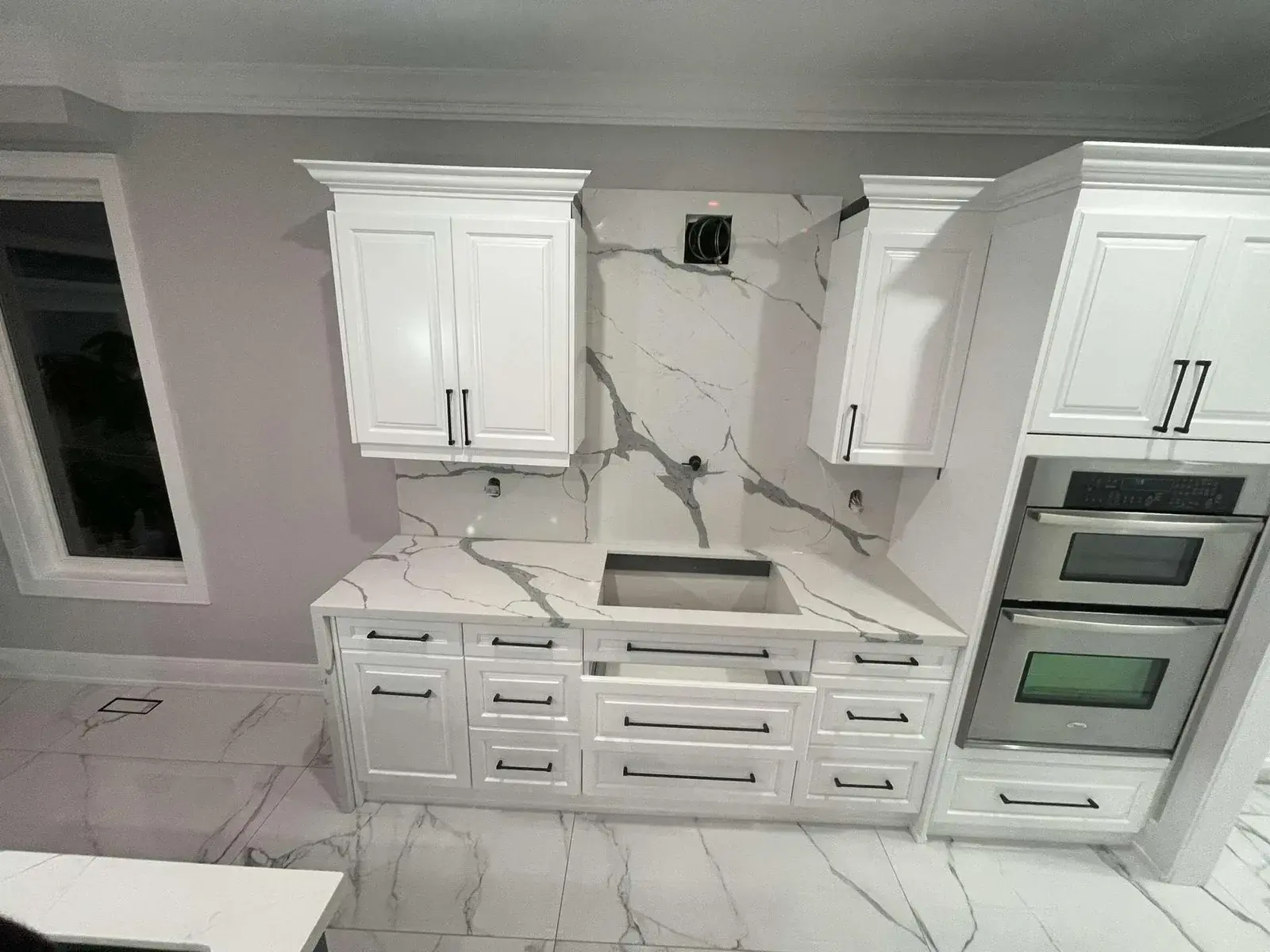White kitchen renovation with a marble-look porcelain floor and wall ovens